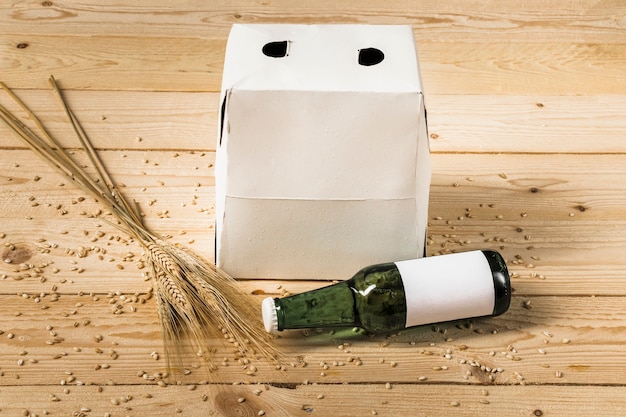 Close-up of carton box; green beer bottle and ears of wheat on wooden backdrop