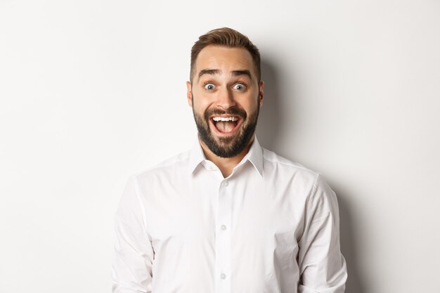 Close-up of caucasian bearded man looking excited, standing amazed against white background.