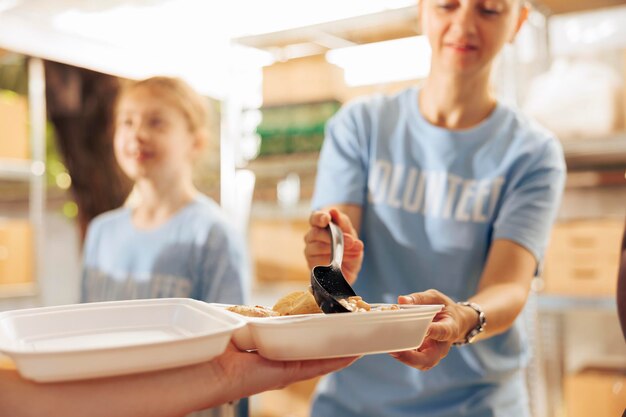 Close-up of a caucasian charity worker handing a person in need a fresh, hot lunch from an outdoor food bank. A detailed view of free food being distributed to the poor and underprivileged.