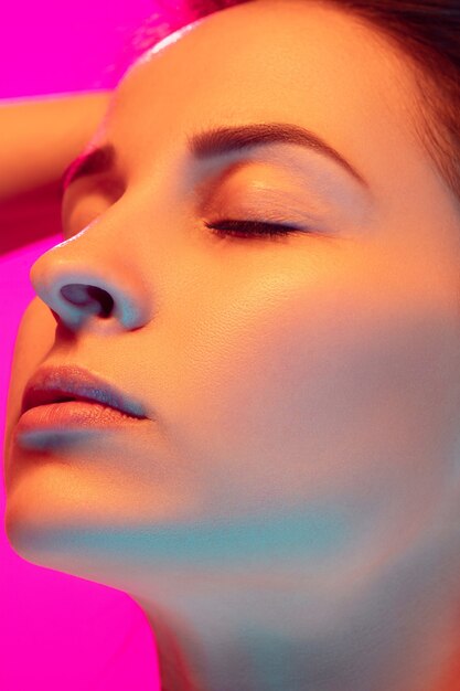 Close up caucasian woman's portrait isolated on pink studio background in mixed neon light. Beautiful female model. Concept of human emotions, facial expression, sales, ad, fashion. Beauty.