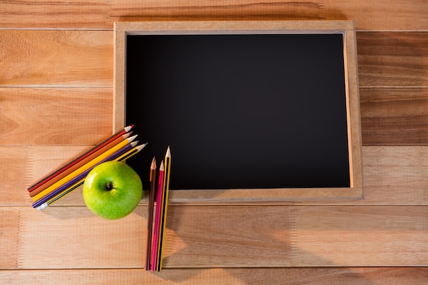 Free photo close-up of chalkboard with colored pencil and apple