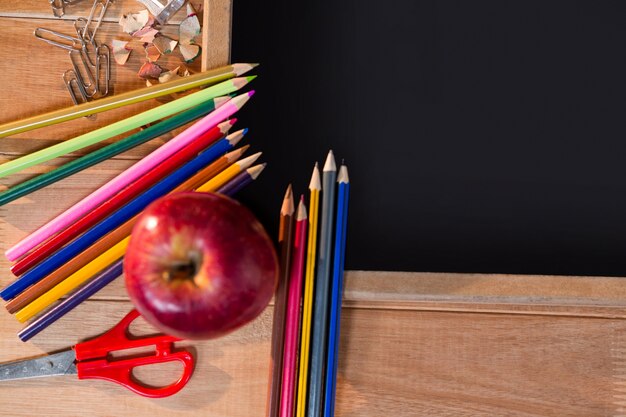 Крупным планом доске с цветными карандашами и яблоком