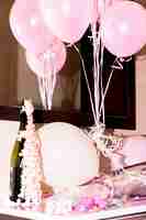 Free photo close-up of champagne bottle with confetti and pink balloons on desk