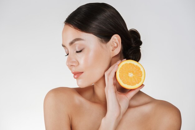 Close up of charming woman with soft fresh skin holding juicy orange, having detox isolated over white