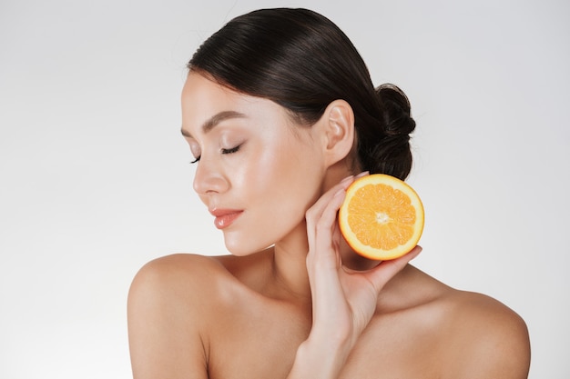 Крупным планом очаровательная женщина с мягкой свежей кожей, держа сочный апельсин, с детокс, изолированных на белом