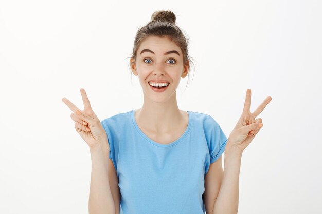 Close-up of cheerful beautiful young woman smiling and showing peace gestures