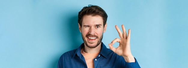 Close up of cheerful and confident bearded man assure everything good showing okay gesture and winki