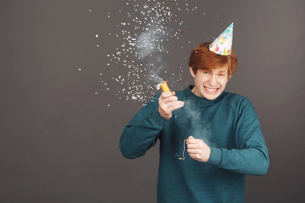 Primo piano di allegro giovane ragazzo dai capelli rossi con taglio di capelli corto in maglione alla moda verde e cappello da festa