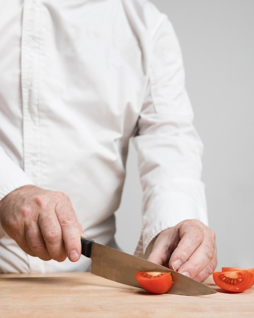 Крупным планом шеф-повар резки помидоры на деревянной доске