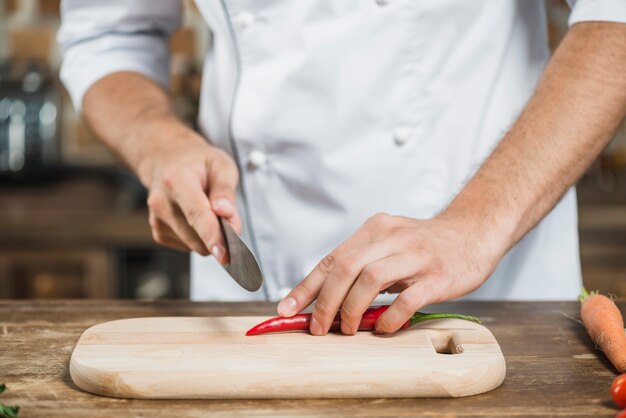 Close-up of chef's hand cutting red chili on chopping board