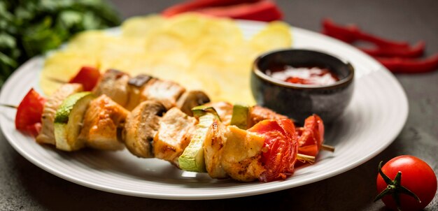 Close-up chicken skewers with sauce and chips