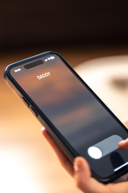父親の着信が表示されている電話を持つ子供の手のクローズアップ