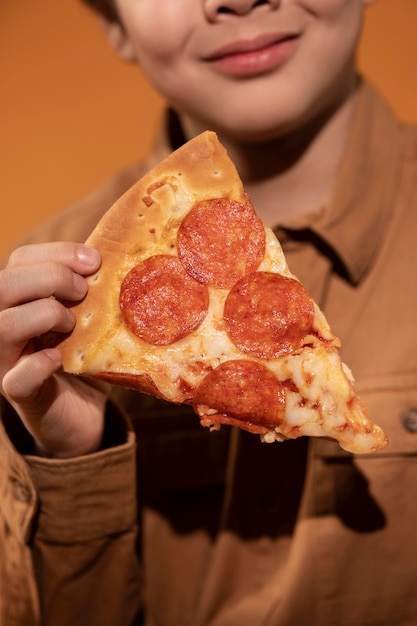 Крупным планом ребенок держит кусок пиццы