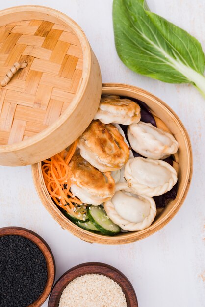 Close-up of chinese steamed dumplings with salad in steamer basket with black and white sesame seeds