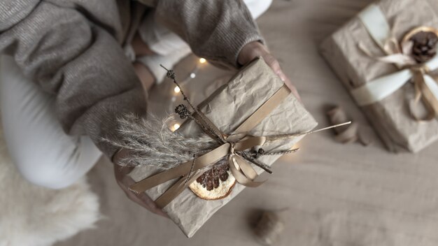 Крупный план рождественского подарка, украшенного засушенными цветами и сухим апельсином, завернутым в крафт-бумагу.