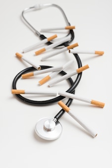 Close-up of cigarettes and stethoscope over white background