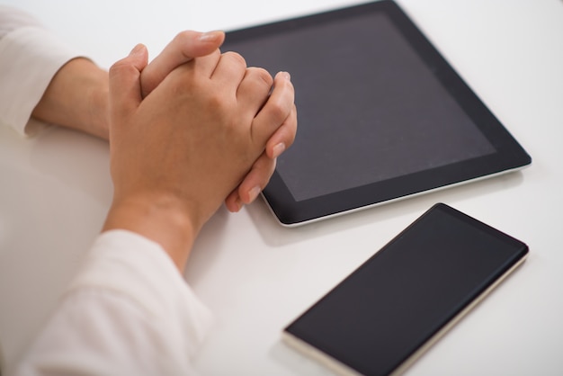 Close-up of clasped hands on table with pc tablet and smartphone