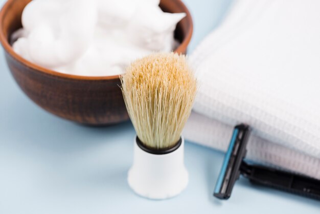 Close-up of classic shaving brush; foam; razor and white napkin on blue backdrop