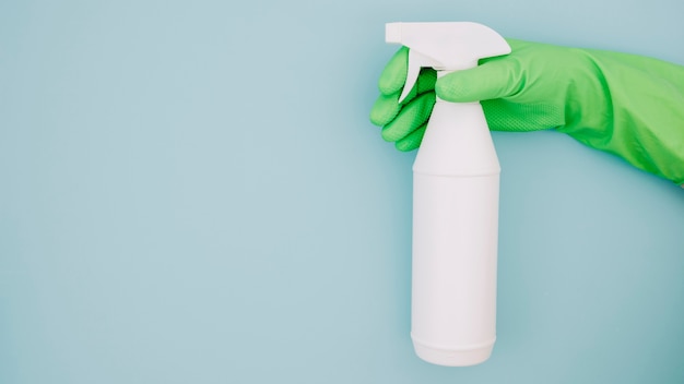 Foto gratuita primo piano della mano del pulitore che indossa i guanti verdi che tengono la bottiglia bianca dello spruzzo sul contesto blu