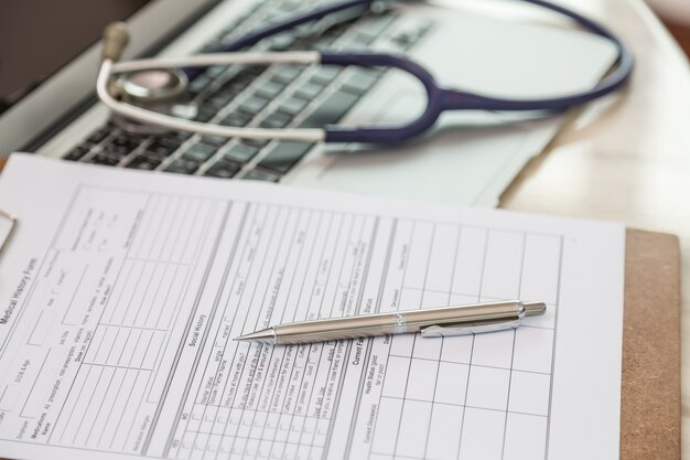 Close-up of clipboard with pen and stethoscope background