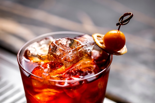 Close up of a cocktail glass with ice cubes garnished with dried lemon and fruit