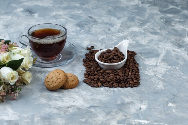 Close-up coffee beans in white porcelain jug with cookies, cup of coffee, flowers