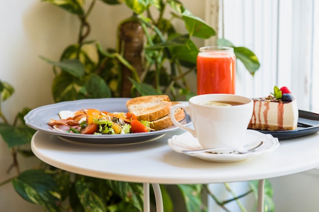 Close-up of coffee; breakfast; cheesecake and red smoothie on white table