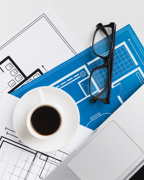 Close-up of coffee cup with blueprints on desk