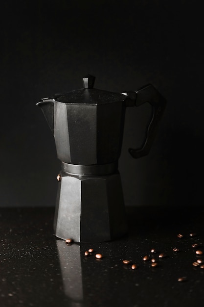 Close-up of coffee maker with roasted coffee beans on black background