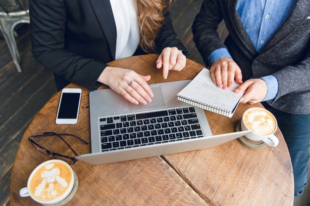 Close-up of a coffee table with two colleagues sitting holding notebook and typing on laptop