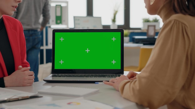사무실에서 업무를 수행하기 위해 노트북에서 녹색 화면을 사용하는 동료들을 닫습니다. 빈 배경에 모의 템플릿과 격리된 크로마 키를 사용하는 동료. 모형으로 작업하는 사람들.
