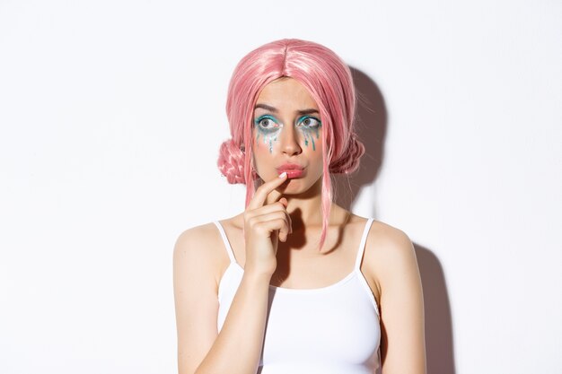 Close-up of concerned cute girl in pink party wig, looking left and thinking, standing in halloween costume.