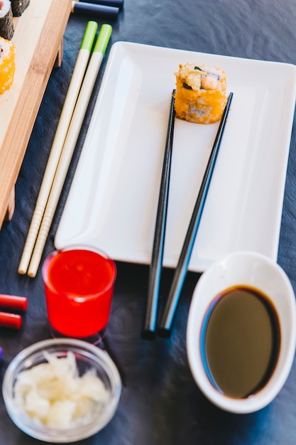 Free photo close-up condiments near chopsticks with roll