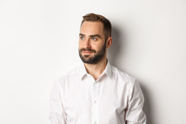 Close-up of confident businessman in white shirt, looking left and smiling satisfied, standing  