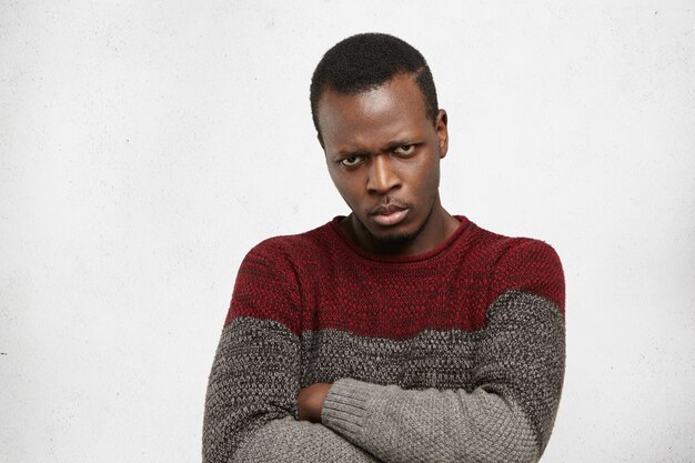 Close up confident young Afro American man keeping arms crossed looking with mad displeased expression, his whole look and posture expressing seriousness of intentions