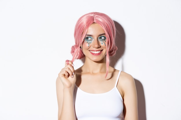 Close-up of coquettish smiling girl in pink wig, looking left intrigued, standing.