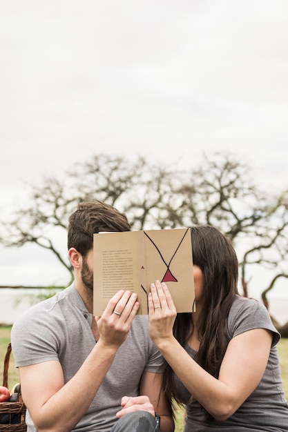 Close-up of couple covering their faces with book