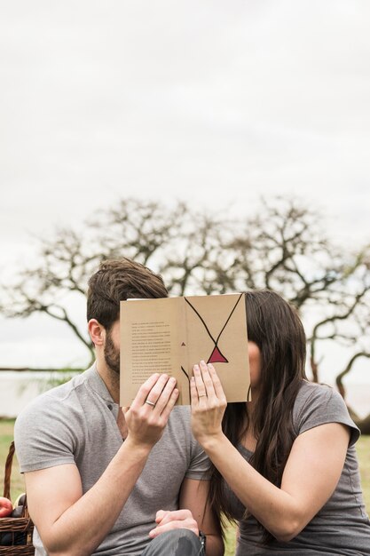 彼らの顔を本で覆うカップルのクローズアップ