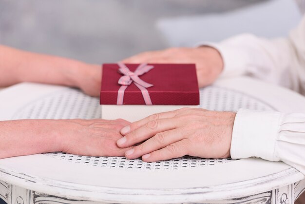 Close-up of a couple holding hands near gift box on table