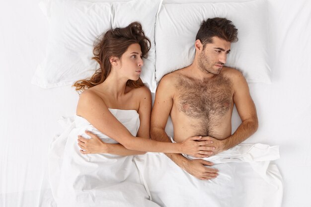 白い毛布の下でベッドに横たわっているカップルのクローズアップ