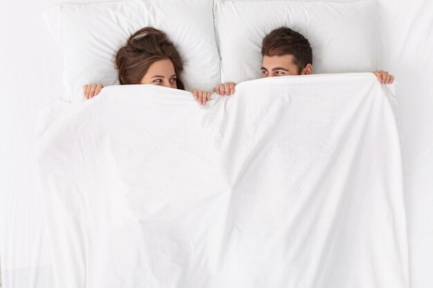Close up on couple lying in bed under white blanket