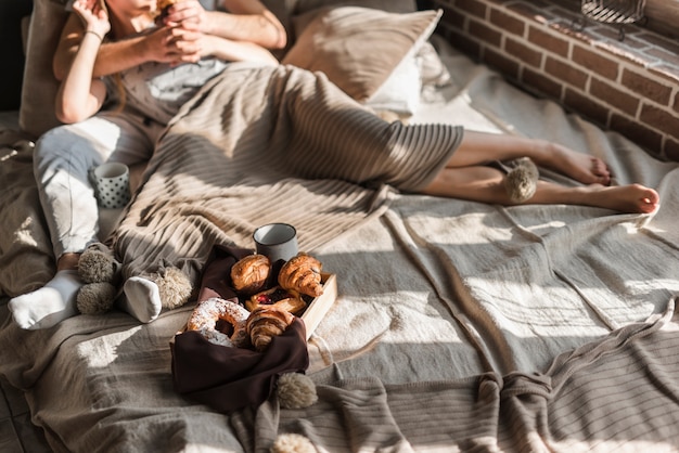 Close-up of couple lying on bed with breakfast