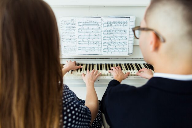 Close-up of couple playing piano with musical sheet