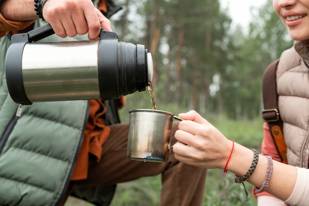 Free photo close-up couple pouring hot drink in nature