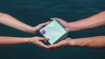 Free photo close-up of a couple's hand holding gift box in front of sea