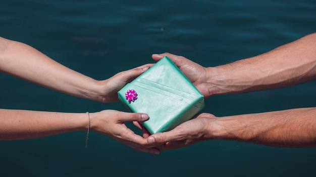 Close-up of a couple's hand holding gift box in front of sea