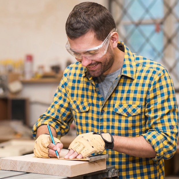 Free photo close-up of craftsman hands in protective gloves measuring wooden block with ruler and pencil