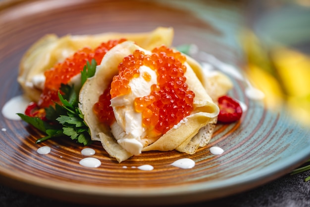 Close up of crepes with red caviar and cream garnished with parsley