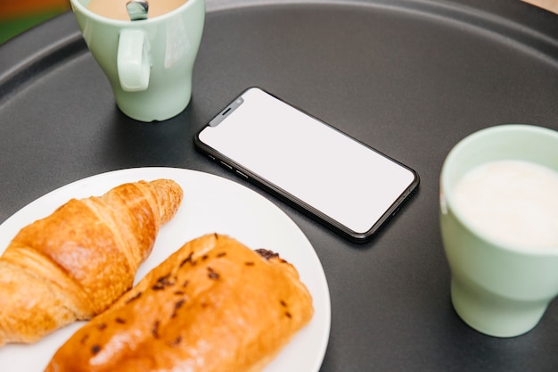 Close-up of croissants, milk and mobile phone at breakfast