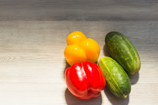 Close-up of cucumber; yellow and red bell peppers on wooden background